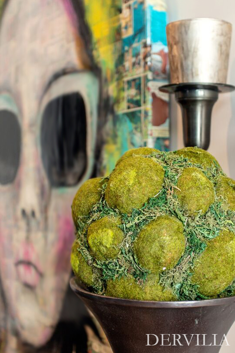 Textural sculptural decor featuring a moss-covered art object in a bowl, styled with metallic candle holders and layered against a bold contemporary artwork, illustrating Dervilia’s curated art and design aesthetic.