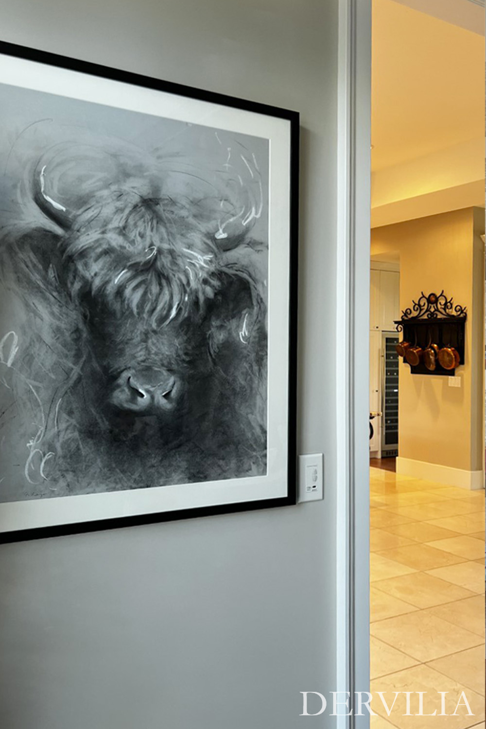Framed monochrome artwork positioned along a hallway opening into a kitchen space, using contrast and placement to create a moment of pause within Dervilia’s art-led interior design.