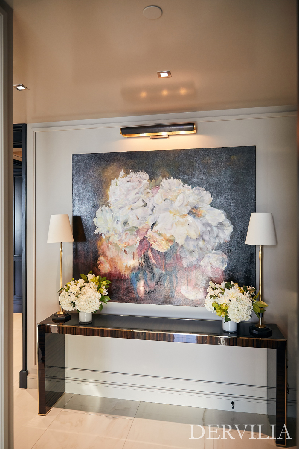 Large-scale abstract floral painting displayed above a polished console table, styled with matching table lamps and white floral arrangements, highlighting Dervilia’s approach to art curation and balanced interior styling.