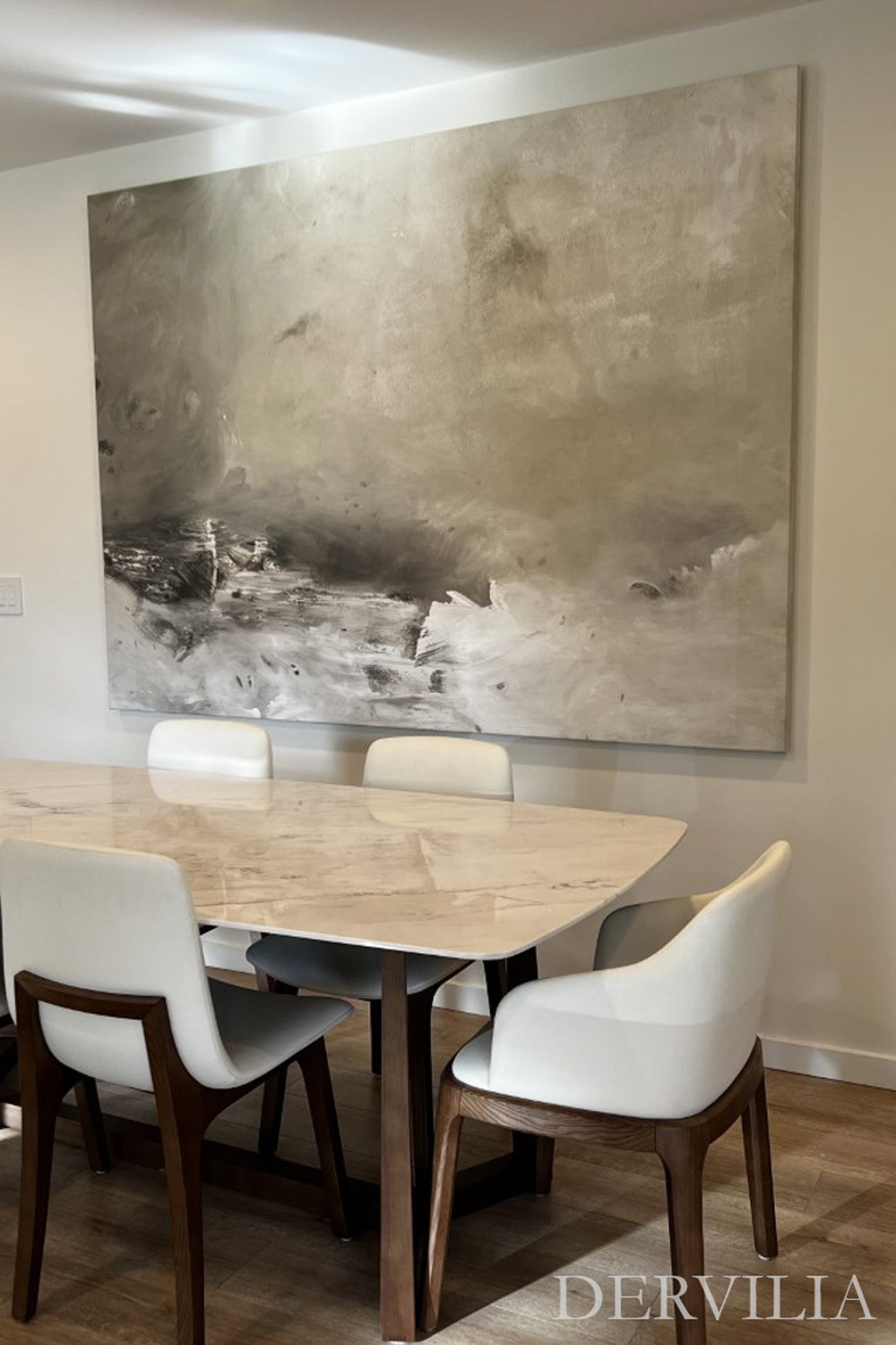 Contemporary dining area featuring a marble table, upholstered chairs, and a large abstract painting as the focal point, reflecting Dervilia’s art-led approach to modern interior composition and balance.