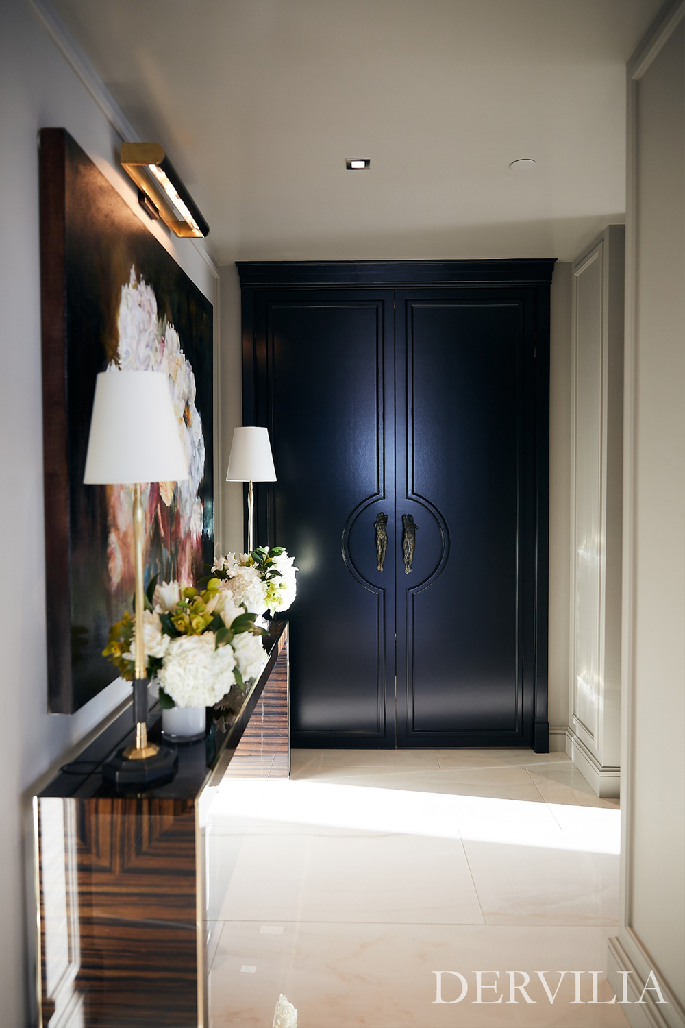 Refined entry hall featuring a large-scale artwork, custom dark cabinetry, and a polished console styled with lighting and florals, expressing Dervilia’s art-driven approach to welcoming, thoughtfully composed interiors.